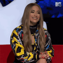 a woman is sitting on a red couch wearing a colorful jacket that says ros