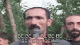 a man with a mustache is speaking into a microphone while another man looks on .