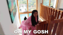 a woman in a pink robe is walking down a set of stairs and says oh my gosh .