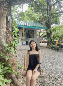a woman sits on a swing in front of a cafe called cafe alava