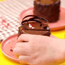 a close up of a person 's hand holding a piece of chocolate cake on a pink plate