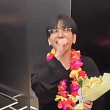a man wearing glasses and a flower lei is holding a bouquet of flowers .