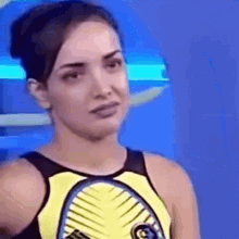 a woman in a yellow tank top is making a funny face while standing in front of a blue wall .