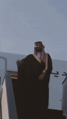 a man waving from the stairs of an airplane with arabic writing on the side