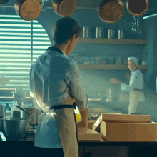 a man in an apron stands in a kitchen looking at a box