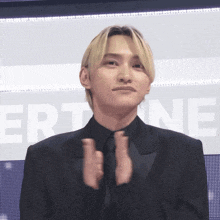 a man in a suit and tie applauds in front of a sign that says ert ne