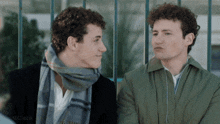 two men are sitting next to each other and one has a scarf on