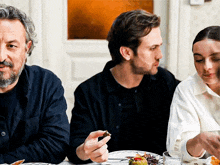 two men and a woman are sitting at a table with plates of food