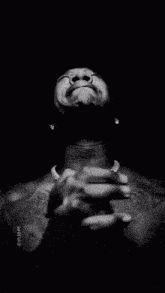 a black and white photo of a shirtless man with his hands folded in front of his face