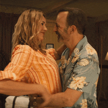 a man in a floral shirt is hugging a woman in an orange shirt