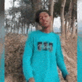 a young man in a blue t-shirt is standing in a forest .