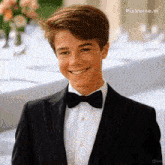 a young man in a tuxedo and bow tie is smiling .