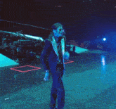 a man in a suit stands on a stage with a cameraman behind him
