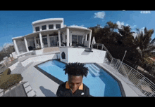 a man in a nike shirt stands in front of a large house with a swimming pool