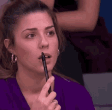 a woman is holding a pen to her mouth and making a funny face .