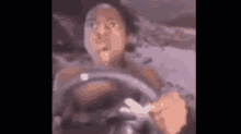 a man is driving a car and making a funny face while holding a steering wheel .