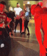 a group of people are standing in a hallway and one of them is wearing a red outfit .