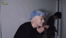 a man wearing a blue hat and a black shirt with the words pow now on it