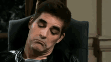 a man is making a funny face while sitting in a chair with his eyes closed .