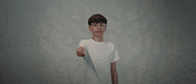 a young boy wearing glasses and a white t-shirt points at the camera