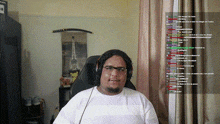 a man wearing headphones and glasses is sitting in front of a screen with a lot of text on it