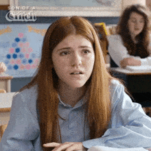 a girl with red hair is sitting at a desk in a classroom with the words son of a grifch behind her