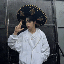 a man wearing a sombrero and a white sweatshirt with the letter m on it is giving a peace sign