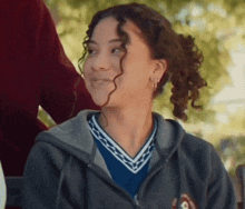 a girl with curly hair is wearing a hoodie and smiling while sitting in a wheelchair .