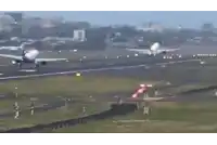 a plane is taking off from a runway with a red and white flag in the foreground