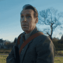 a man in a suit and tie is standing in a field with trees in the background