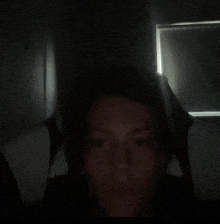 a person 's face is visible in the dark with a window behind them