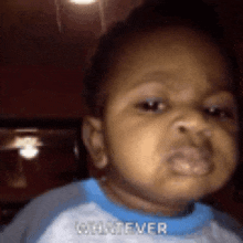 a baby in a blue shirt is making a funny face and says whatever .