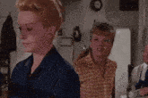 a woman in a blue shirt is standing next to another woman in a yellow plaid shirt in a kitchen .