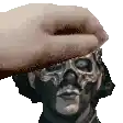 a hand is holding a statue of a man 's head with a skull on it .