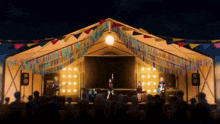 a group of people are standing in front of a stage with a yellow tent behind them