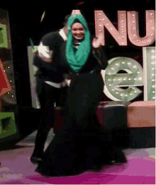 a woman wearing a green hijab is dancing with a man in front of a sign that says nu