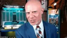 a bald man in a suit and tie is sitting in front of an arcade machine .
