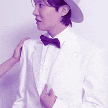 a man in a white suit and purple bow tie has a woman 's hand on his shoulder