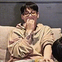 a man wearing glasses is sitting on a couch and eating a piece of food .