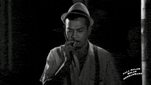 a black and white photo of a man wearing a hat and suspenders with kala malam mengambang written below him