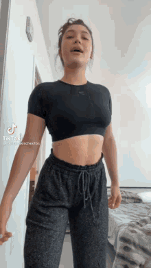 a woman in a black crop top and gray sweatpants is standing in a room .