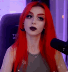a woman with red hair is sitting in front of a microphone and looking at the camera .