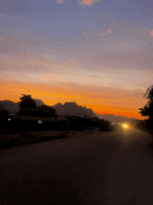 a sunset with mountains in the background and a car driving down the road