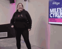 a woman standing in front of a sign that says miley cyrus