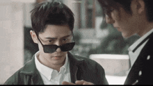 a man wearing sunglasses looks at another man 's cell phone