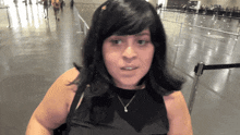 a woman wearing a black top and a necklace stands in an airport