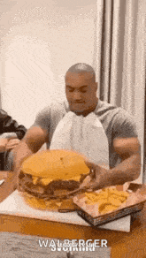 a man is sitting at a table eating a very large hamburger and french fries .