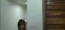 a woman is standing in a hallway next to a wooden door and stairs .