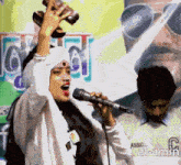 a woman singing into a microphone in front of a man wearing a shirt that says assic al-amin