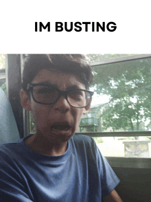 a boy with glasses is making a funny face with the words im busting behind him